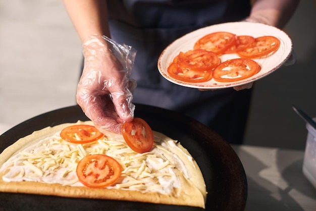 Chef manteniendo el plato con tomate cortado Mano de mujer poniendo rodajas de tomate en panqueque lubricado con salsa Vista frontal