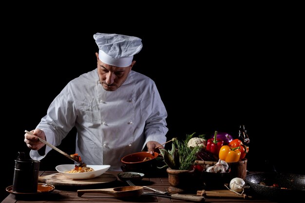 Chef masculino com uniforme branco prepara espaguete com legumes no prato antes de servir enquanto trabalha na cozinha de um restaurante