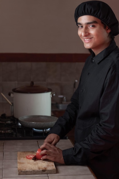 Chef masculino cortando um tomate vermelho fresco na placa de madeira rústica com uma faca na cozinha