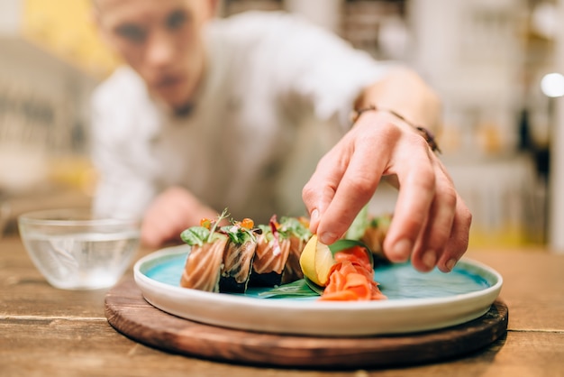 Foto chef masculino cozinhando rolos de sushi, processo de preparação de comida japonesa