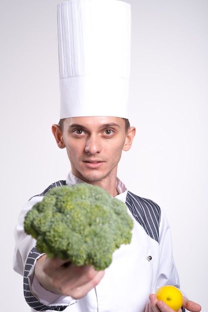 Chef masculino cozinheiro homem de camisa uniforme branca posando isolado no retrato de estúdio de parede branca. Cozinhar o conceito de comida. Simule o espaço da cópia. Brócolis e um limão nas mãos do cozinheiro close-up em um branco