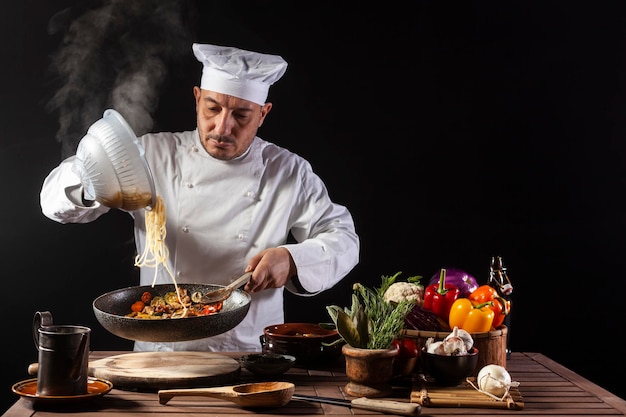 Chef masculino de uniforme branco derramando espaguete cozido em panela wok para cozinhar macarrão com legumes