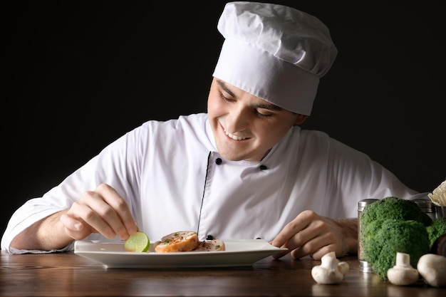 Chef masculino de uniforme enfeitando prato saboroso contra fundo preto