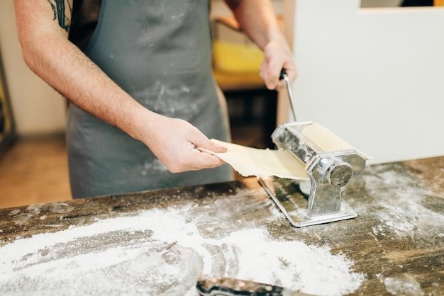 Chef masculino en delantal trabaja con máquina de pasta