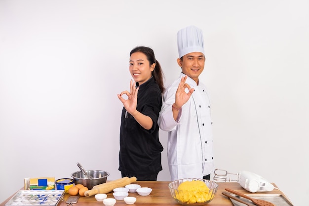 Chef masculino e feminino com gesto bem atrás da mesa de cozinha