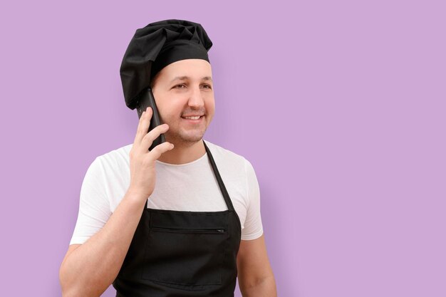 Chef masculino sonriente usando teléfono móvil sobre fondo de estudio púrpura el concepto de cocina