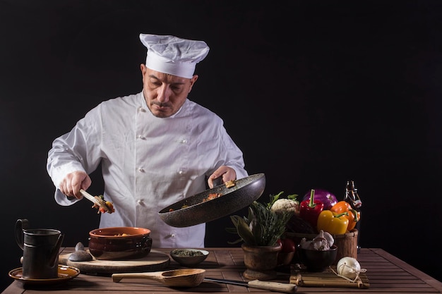 Chef masculino en uniforme blanco preparando plato de comida con verduras