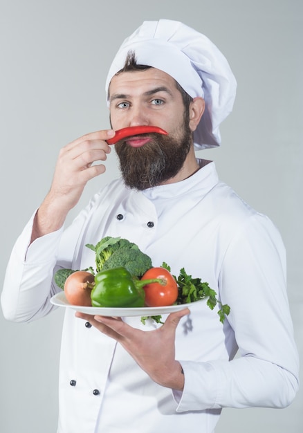 Chef masculino en uniforme blanco sostiene pimienta al lado de la cara concepto de cocina y nutrición saludable barbudo