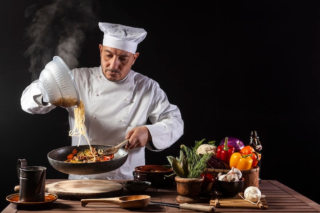 Chef masculino en uniforme blanco vertiendo espaguetis hervidos en pan wok para cocinar pasta con verduras