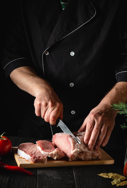 Chef Metzger schneidet Schweinefleisch mit Messer in der Küche und kocht Essen. Gemüse und Gewürze auf dem Küchentisch um ein leckeres Mittagessen zuzubereiten