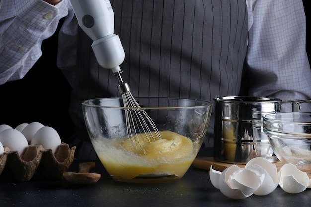 Chef mit Mixer in den Händen kochen Kuchen mit Zutaten auf dem Tisch