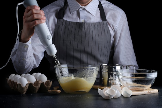 Chef mit Mixer in den Händen kochen Kuchen mit Zutaten auf dem Tisch