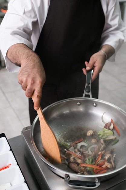 Chef mostrando suas habilidades profissionais. Cozinhar mestre no trabalho na cozinha do restaurante. Legumes e carne misturados na técnica do ar