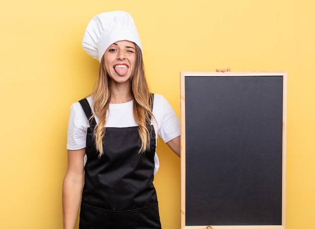 Chef mujer con actitud alegre y rebelde, bromeando y sacando la lengua. concepto de menú de pizarra