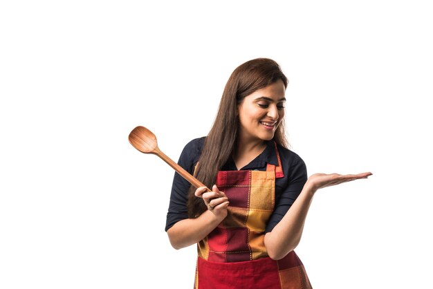 Chef mujer india o asiática con delantal y sosteniendo una espátula de madera mientras está de pie aislado sobre fondo blanco.