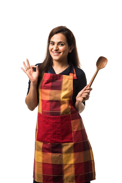 Chef mujer india o asiática con delantal y sosteniendo Pan y espátula mientras está de pie aislado sobre fondo blanco.