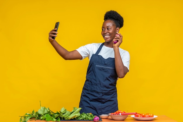 Chef mujer negra haciendo un video mientras sostiene algunas cebollas, con otros ingredientes frente a ella en un escritorio