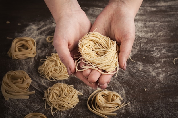 Chef mujer sosteniendo el nido de tallarines en las manos, fondo de la mesa de la cocina. Preparar pasta italiana casera, espacio de copia