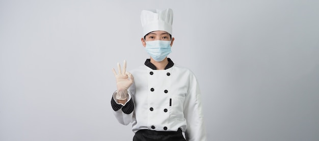 Chef mulher asiática em uniforme de cor branca com produtos higiênicos, como máscara facial médica e mãos de borracha