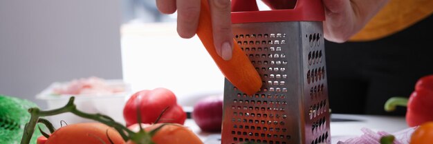 Chef mulher ralando cenouras na mesa com vegetais closeup