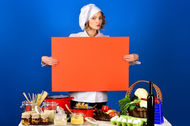 Chef mulher segura placa vermelha para texto preparação de alimentos chef mulher séria senta-se à mesa, copie o espaço para