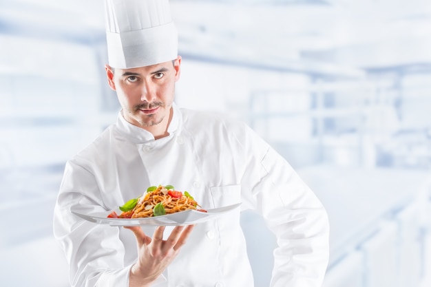 Chef na cozinha do restaurante, segurando o prato com refeição italiana espaguete à bolonhesa.