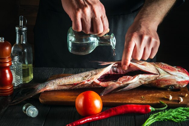 Chef o cocinero prepara pescado fresco carpa cabezona con vinagre. Preparación para cocinar arenque. Entorno de trabajo en la cocina del restaurante o cafetería.