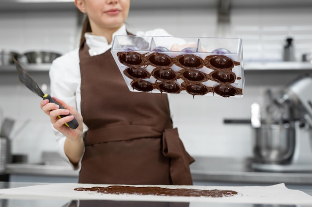 Foto chef ou chocolatier faz chocolates doces em uma cozinha profissional ela vira o molde