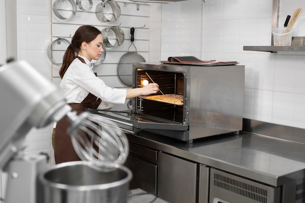 Chef pastelera pone la masa de bizcocho en el horno y comprueba la masa con un palo de madera