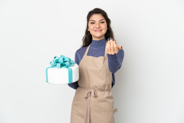 Chef de pastelería rusa sosteniendo un gran pastel aislado en la pared blanca que invita a venir con la mano. Feliz de que hayas venido