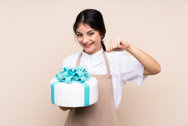 Chef pastelero mujer sosteniendo un gran pastel sobre pared aislada orgulloso y satisfecho de sí mismo