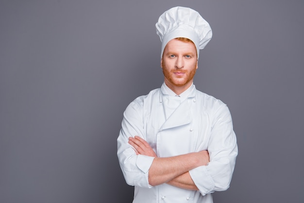 Chef pelirroja en uniforme posando contra la pared gris