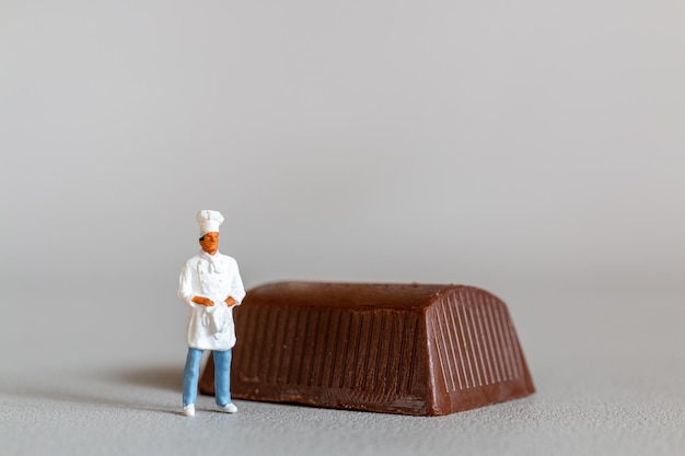 Chef de personas en miniatura con chocolate de pie mientras está de pie contra un fondo gris