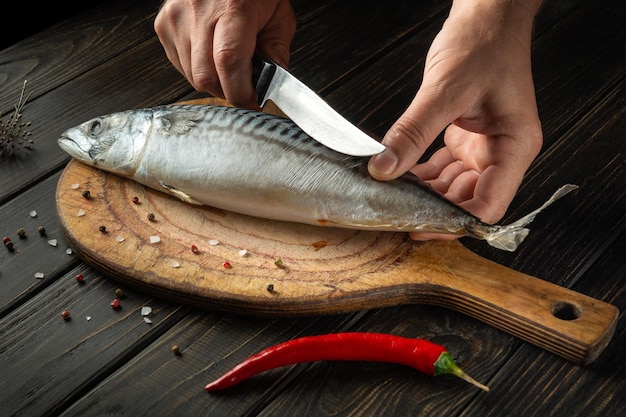 Chef de pescado corta scomber con un cuchillo en la tabla de cortar de la cocina antes de cocinar con especias y pimienta