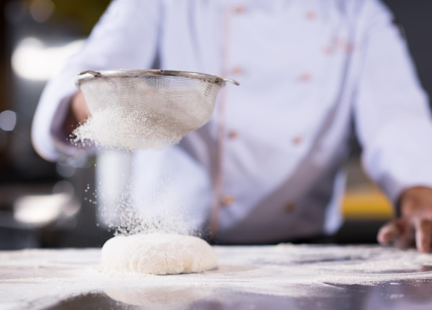 chef polvilhando farinha sobre massa de pizza fresca na mesa da cozinha