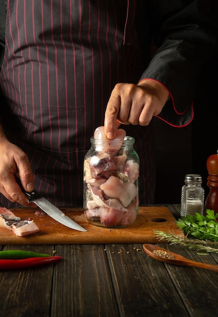 El chef pone filetes con pescado crudo en un frasco el concepto de salar o enlatar pescado en casa con especias y cilantro en casa