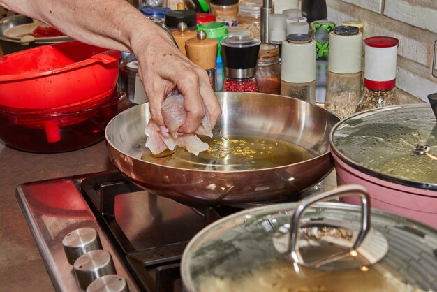 El chef pone pedazos de pecho de pollo en la sartén en la estufa de gas