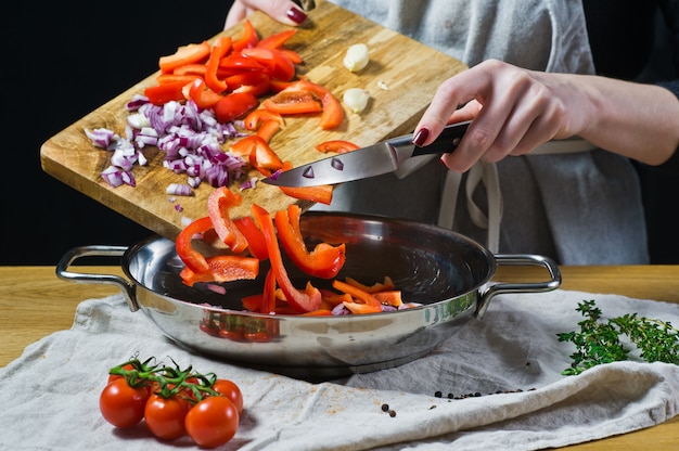 El chef pone pimientos rojos picados y cebollas con un cuchillo en la sartén.