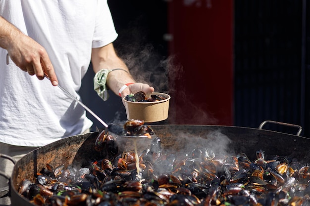 Chef poniendo deliciosos mejillones hervidos en una caja para llevar cocinando mariscos en el festival de comida callejera