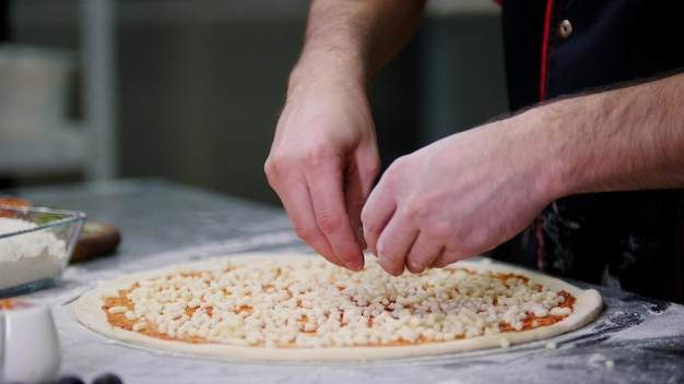 Un chef poniendo queso en la pizza alineando la capa de queso en la pizza