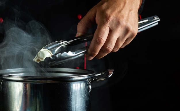 El chef prepara albóndigas en la cocina en una olla el concepto de un delicioso almuerzo en un fondo oscuro herramienta de cocina en la mano del cocinero