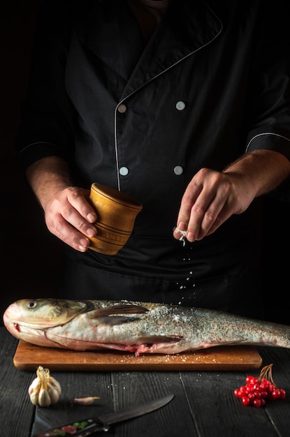 El chef prepara arenque de carpa plateada en la cocina del restaurante El cocinero echa sal al pescado