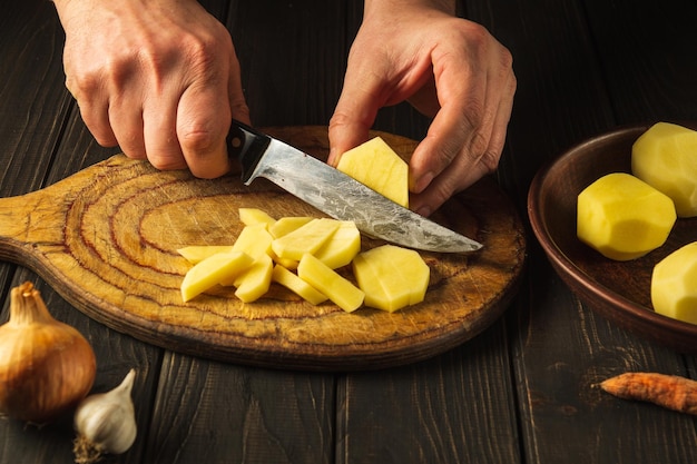 Chef prepara batatas cruas para almoço ou jantar Closeup de mãos de cozinheiro enquanto trabalhava em uma cozinha