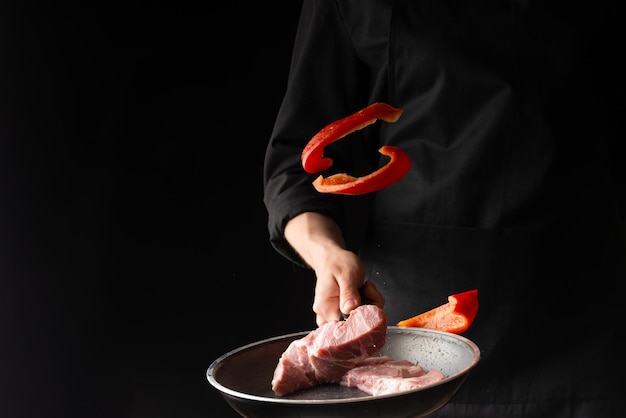 Chef prepara bifes de carne de porco ou carne bovina jogando carne fresca com pimentão em uma chapa em um fundo preto horizontal foto menu livro de receitas restaurantes comida saborosa