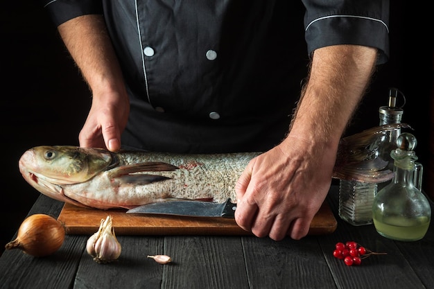 El chef prepara carpa plateada en la cocina del restaurante Preparación para cortar pescado con un cuchillo