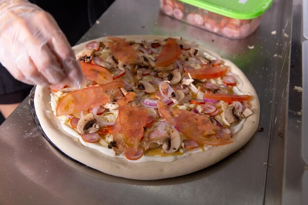 Foto el chef prepara una clásica pizza italiana con salchichas, setas y tomates.