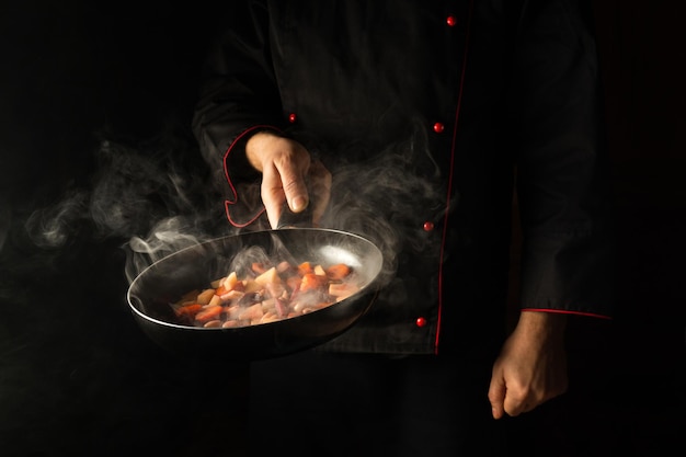 Chef prepara comida en una sartén con vapor sobre un fondo negro