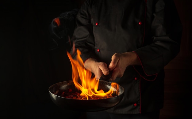 El chef prepara comida vegetal en una sartén con una llama de fuego.