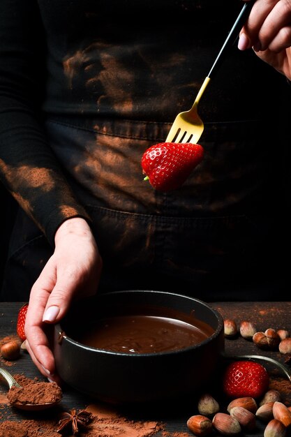 El chef prepara fresas en chocolate sobre un fondo negro Preparación de postre de chocolate