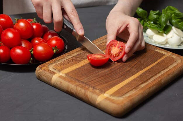 Chef prepara ingredientes para pizza de queso casera Manos cortan tomate cherry con cuchillo